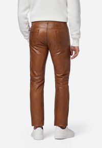 Bruine leren broek met achterzakken, gladde textuur, recht model en zichtbare stikseldetails. Draag met witte sneakers.