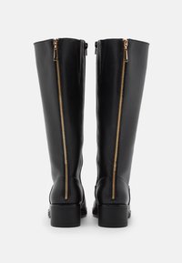 Bottes en cuir noir, hauteur genou, avec des zips dorés à l'arrière, présentant une texture lisse et des talons blocs.