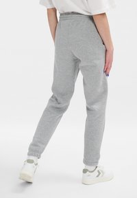 Graue Sweatpants aus weichem Material mit schmal zulaufendem Design, elastischem Bund und Bündchen. Kombiniert mit weißen Sneakers mit grünen Akzenten.