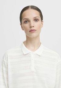 Witte polo shirt, gebreid met horizontale strepen, met een klassieke kraag en een drie knoopsluiting. Licht en ademend materiaal.