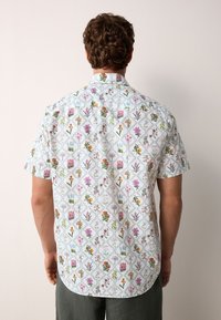 Chemise à manches courtes en tissu léger, avec un fond blanc orné d'un motif floral coloré et un ourlet arrondi.