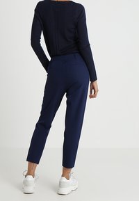 Mörkblå byxor med avsmalnande ben, tillverkade av ett mjukt tyg. Har två bakfickor och en medelhög midja. Kombineras med vita sneakers.