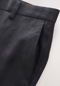 Pantaloni in tessuto nero con superficie strutturata, dotati di una vita piatta e una tasca laterale; design sartoriale con linee pulite.