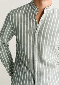 Camisa a rayas con cuello mao, que presenta rayas verticales verdes y blancas, confeccionada en una tela ligera, con cierre de botones en la parte delantera.