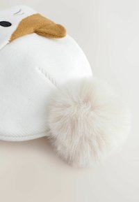 Biała czapka robiona na drutach z brązowymi akcentami, z puszystym białym pomponem z tyłu i prostymi ściegami z przodu.