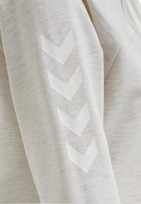 Felpa grigia chiara con texture morbida, con quattro applicazioni a forma di chevron bianche lungo la manica sinistra disposte in modo verticale.