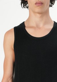 Musta ribattu hihaton toppi, joka on valmistettu puuvillasekoitteesta. Sisältää pyöreän kaula-aukon ja sleeveless-muotoilun, joka korostaa tiukkaa siluettia.