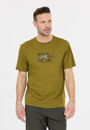 Mann trägt ein olivgrünes T-Shirt mit einer Grafik eines Geländewagens und Bäumen, steht vor einem schlichten weißen Hintergrund.