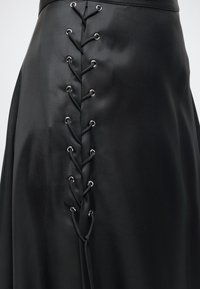 Μαύρη σατινέ φούστα με κάθετη δαντέλα με μαύρο κορδόνι που περνά από ασημένια οπτικά στη μέση μπροστά.