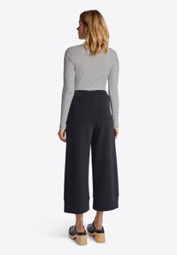 Zwarte wijde culottes met een gladde textuur en een elastische tailleband, gecombineerd met een zwart-wit gestreepte lange mouw top en houten klompen.