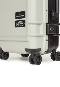 Valigia rigida con ruote di colore grigio chiaro e dettagli neri, dotata di chiusure con doppia zip, di una serratura TSA e di quattro ruote robuste per una facile mobilità.