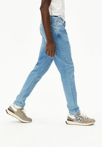 Hellblaue Skinny-Jeans aus Denim mit Gesäßtaschen und kontrastierenden Nähten. Kombiniert mit grauen und weißen Sneakern.