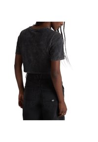 Camiseta negra recortada con una textura desvanecida y escote redondo, combinada con jeans de mezclilla negros de cintura alta con bolsillos traseros visibles.