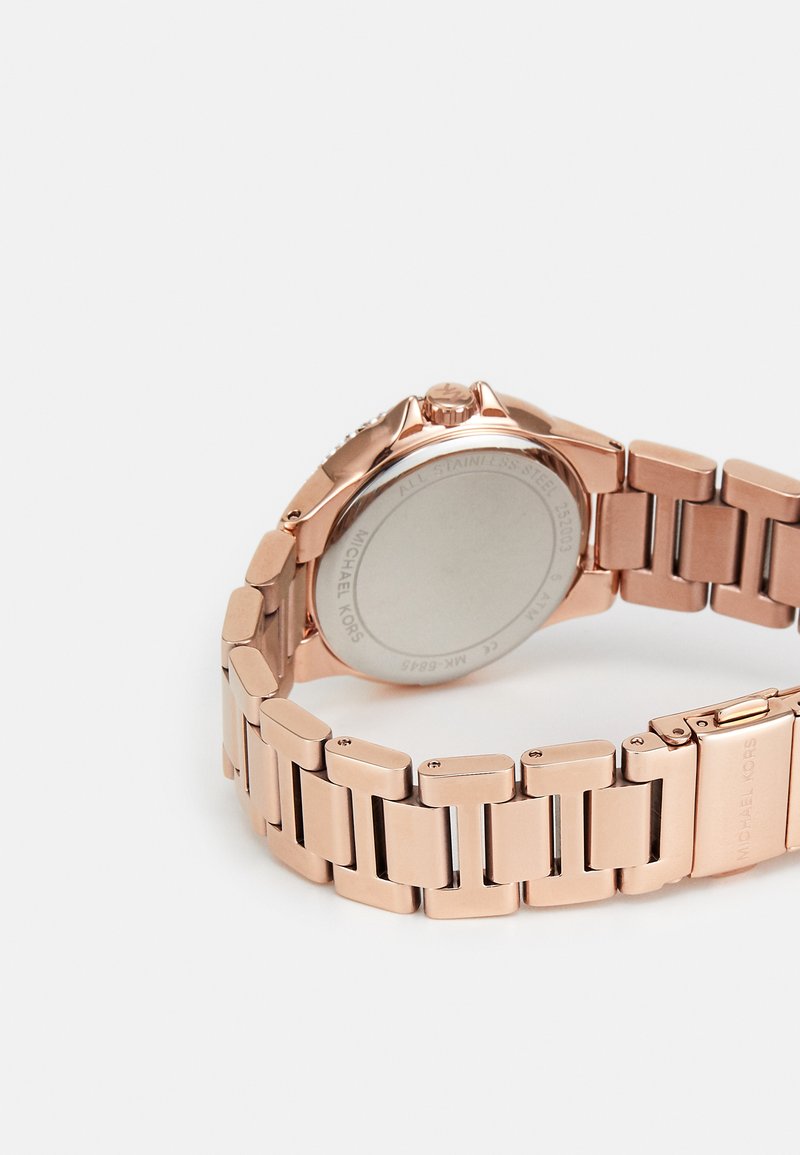 Roségoldene Metalluhr mit einem Gliederarmband, strukturierten Details auf der Lünette und einem glatten, runden Gehäuse. Rückseite mit eingraviertem Markennamen.