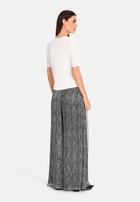 White short-sleeve top paired with wide-leg black and silver pleated trousers, displaying a soft texture and flowing design.