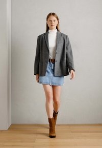 Blazer en laine gris, col roulé blanc, jupe en jean bleu clair, ceinture en cuir marron et bottines à talons marron. Textures lisses et coupe ajustée.