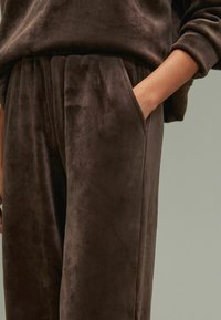 Bruine corduroy broek met een zachte textuur, elastische tailleband en zijzakken. Eenvoudig en losvallend ontwerp, gedeeltelijk getoond met hand in de zak.