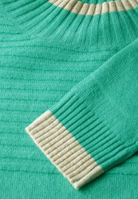 Turkusowy sweter robiony na drutach z prążkowanym wzorem, z kremowym, paskowanym okrągłym dekoltem i mankietami. Miękka tekstura z subtelnym wzorem.