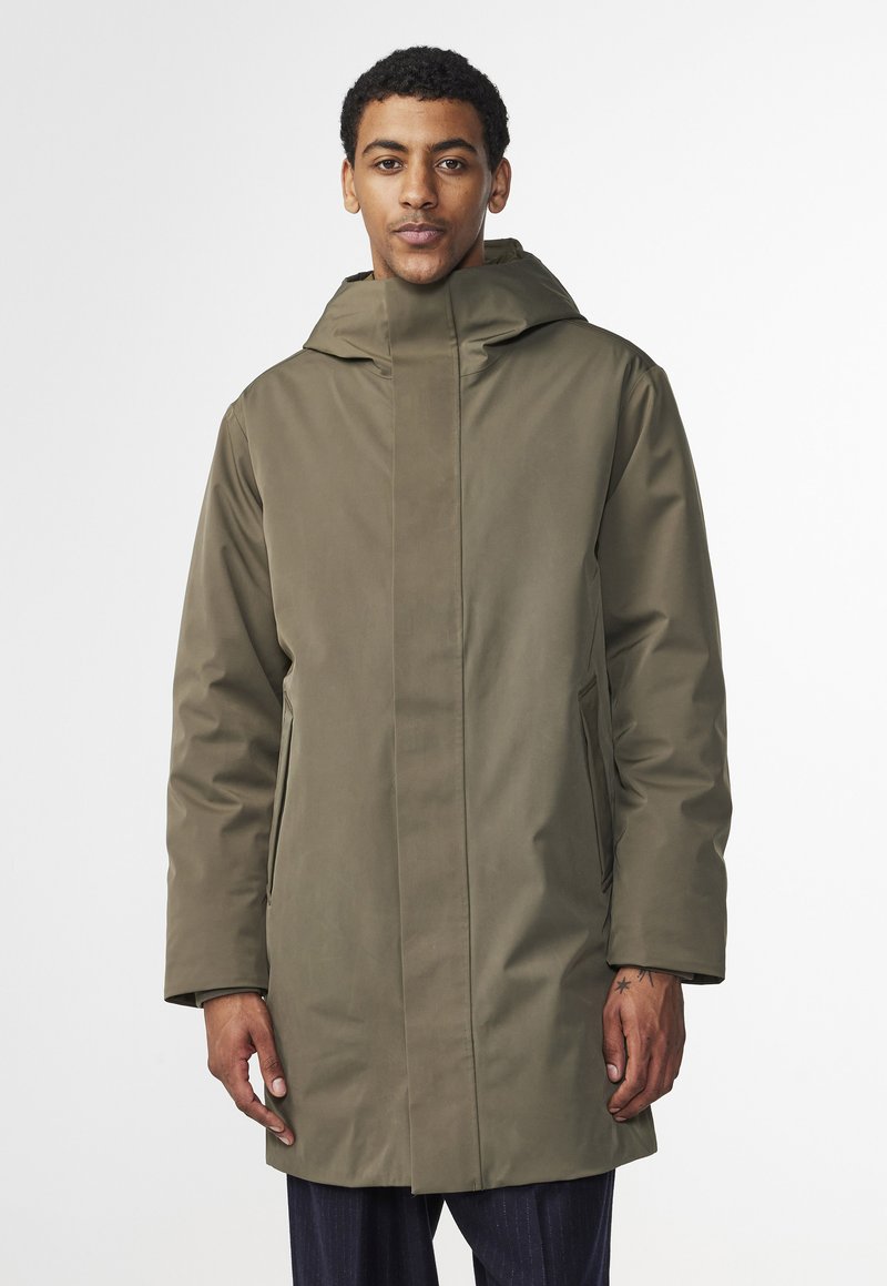 Olivgrön vattentät parka med hög krage, huva, framdragkedja och snedställda sidofickor. Slät textur och rak passform.