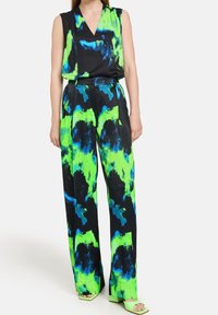 Combinaison sans manches noire, ornée de motifs abstraits verts et bleus. Coupe ample avec un décolleté en V profond. Associée à des talons verts assortis.