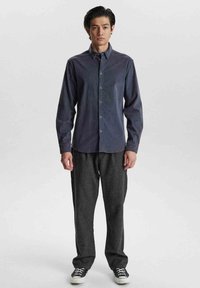 Langärmliges marineblaues Hemd mit Knopfleiste, kombiniert mit lockeren dunkelgrauen Hosen und schwarzen Sneakers, im entspannten Schnitt und aus strukturiertem Stoff.