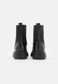 Botas negras hasta el tobillo con un trasero de cuero liso y un eje de tela elástica, equipadas con asas de tirón y suelas gruesas y resistentes.
