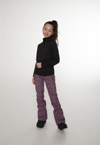 Haut noir à manches longues avec col zippé, associé à un pantalon de neige rose orné d'un motif léopard noir. Des bottes noires complètent la tenue.