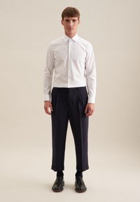Weiße Knopfleiste-Hemd und marineblaue Plissee-Hosen, mit dunklen Schuhen. Glattes Baumwollmaterial, klassischer Kragen, taillierte Passform und verkürzter Saum bei den Hosen.