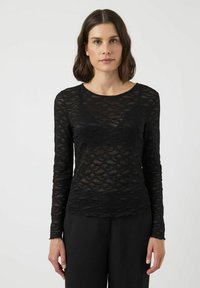 Svart spets topp med långa ärmar och ett vågmönster, med rund halsringning och en åtsittande silhuett. Texturerad, semi-genomskinlig tyg.