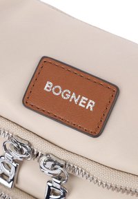 Borsa in nylon beige con etichetta in pelle marrone con la scritta "BOGNER" in rilievo. Chiusura con cerniera argentata e design intrecciato. Texture liscia.