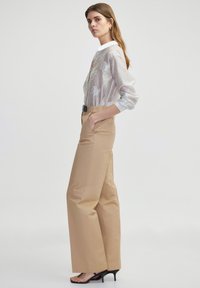 Camisa de rayas gris claro con bordado floral, combinada con pantalones de pierna ancha beige de cintura alta y sandalias negras de tacón.