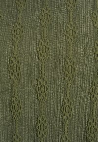 Zelená tkanina s texturou, kterou tvoří vertikální linky a květinové vzory, představující žebrovaný povrch a složité detaily.