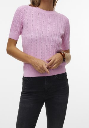 Osoba ubrana w jasnofioletową, krótkorękawową dzianinową bluzkę z teksturowanymi, pionowymi wzorami oraz czarne spodnie, uzupełniona bransoletką w kolorze żółwia.