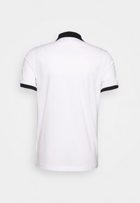 Valkoinen polo-paita, jossa on musta kaulus ja hihansuut, lyhyet hihat ja suora helma. Valmistettu sileästä, teksturoidusta kankaasta.