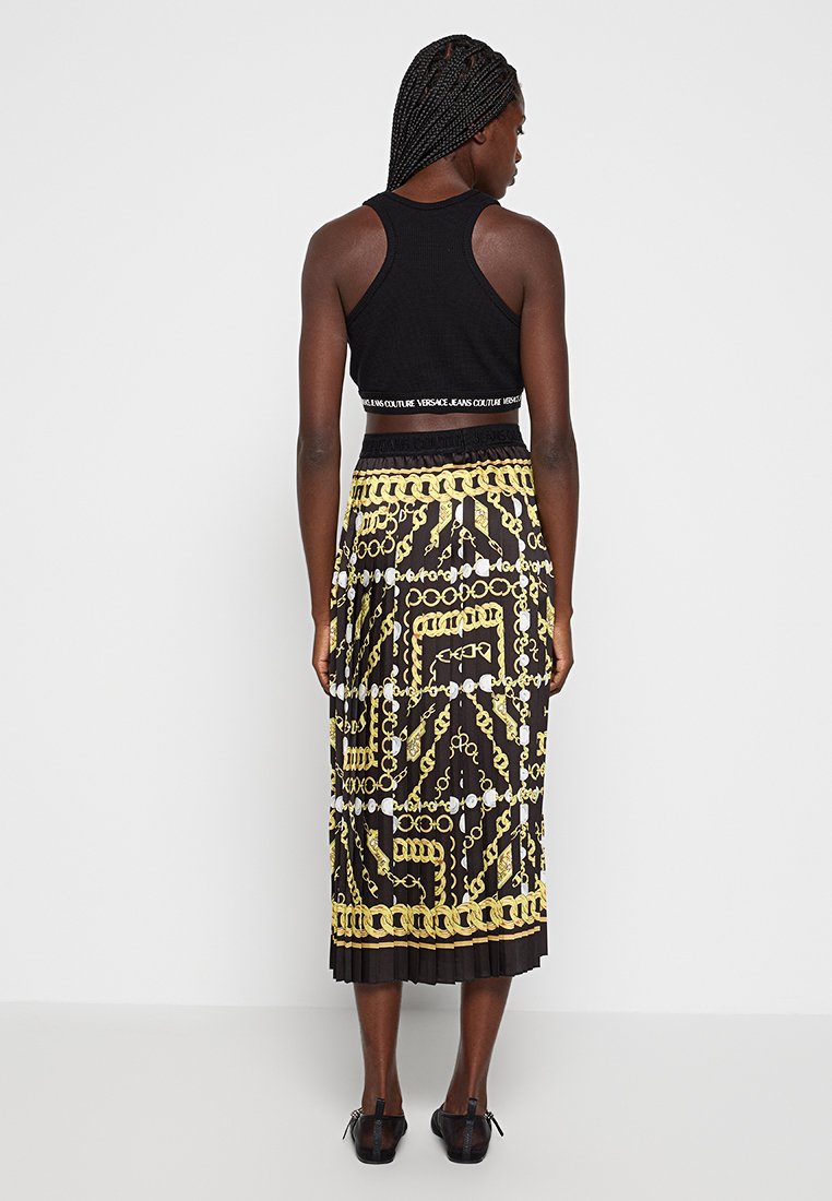 Crop top noir à côtes avec une bande logo, associé à une jupe midi plissée ornée de motifs de chaînes dorées audacieux sur fond noir.