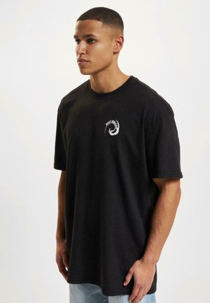 T-shirt en coton noir à manches courtes, arborant un logo blanc circulaire à l'avant. Le design est décontracté avec un col rond.