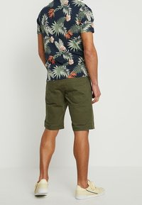 Camisa de hombre de manga corta, color azul marino con estampado floral en verde, naranja y blanco. Pantalones cortos de color verde oliva, de corte casual, con bolsillos y dobladillos enrollados.