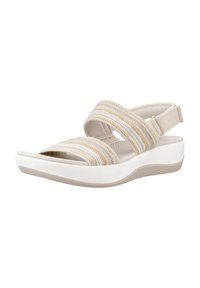 Sanda en tela beige con correas elásticas, un respaldo ajustable y una suela de plataforma blanca acolchada. Presenta una textura suave y un diseño minimalista.