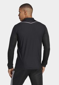 Mustega pikkade varrukatega spordipoloo, millel on tekstuuriga muster, slim fit lõige, krae ja valge aktsent seljaõmblusel.