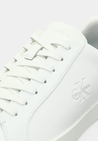 Baskets en cuir blanc avec lacets texturés, branding discret sur le côté et finition lisse. Présentent un design minimaliste et un bout arrondi.