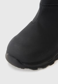 Botas negras impermeables con puntera redondeada, textura suave y suela resistente con un patrón de relieve profundo para una mejor tracción.