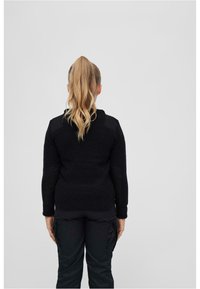 Maglione nero in maglia con tessuto testurizzato, design aderente e dettagli sulle spalle. Indossato con pantaloni cargo scuri e larghi, visto da dietro.