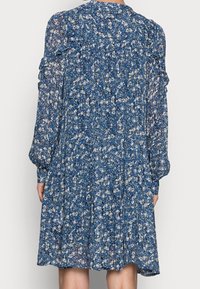 Blaues Blumenkleid aus leichtem, transparentem Stoff. Es hat lange Ärmel, Rüschelemente und ein gerafftes Rockdesign.