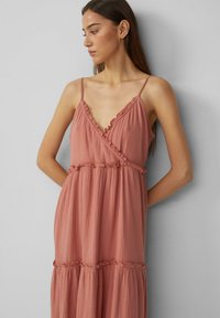 Langes, pinkes Baumwollkleid mit tiefem V-Ausschnitt und Rüschendetails. Verfügt über verstellbare Spaghettiträger und ein gestuftes Rockdesign.