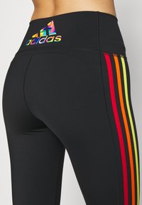 Leggings atletici neri con un alto punto vita, strisce multicolori in rosso, arancio e giallo, e un logo Adidas riflettente sul retro.
