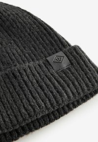 Schwarze, gerippte Strickmütze aus Wolle, ausgestattet mit einem rechteckigen Lederpatch mit einem aufgenähten Logo auf der Vorderseite.