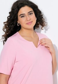 T-shirt rosa chiaro a V con maniche corte, realizzato in un tessuto liscio. Presenta una delicata cucitura lungo il collo.