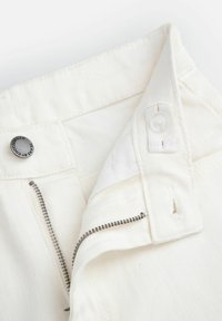 Kieszonka białych dżinsów z metalowym suwakiem, guzikiem z napisem marki oraz białym wnętrzem z materiału. Teksturowany i strukturalny design.