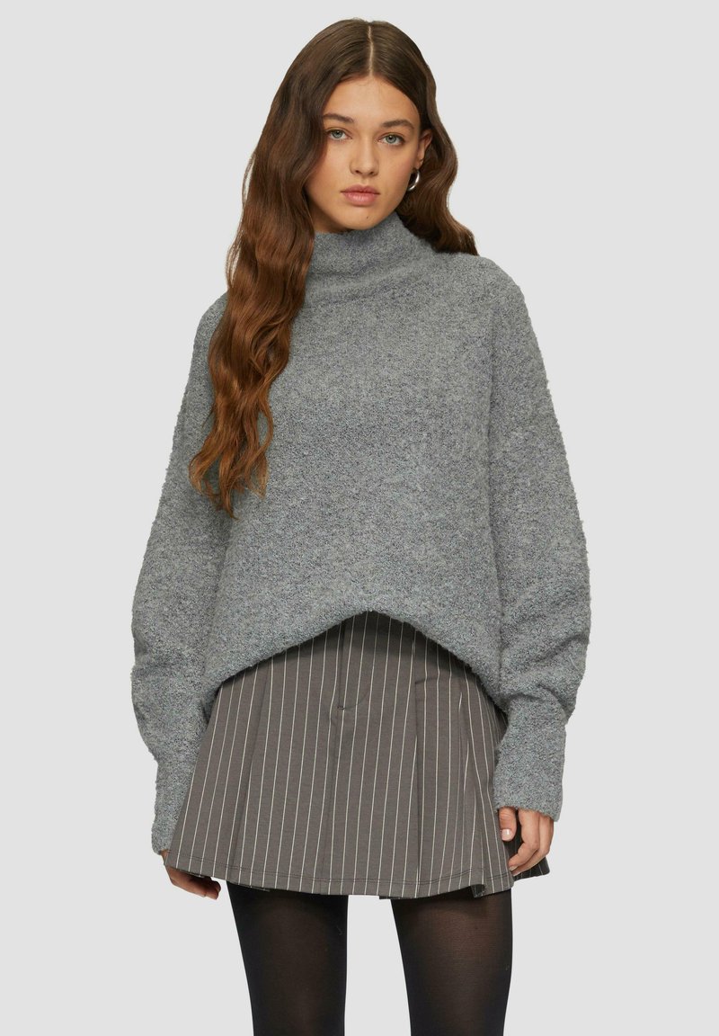 Hellgrauer, strukturierter Pullover mit lockerer Passform und hohem Kragen, kombiniert mit einem gestreiften grauen Rock. Verfügt über lange Ärmel und einen gekürzten Saum.