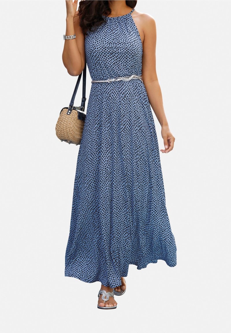 Vestido maxi en azul con un patrón de lunares. Presenta un diseño de escote halter, una cintura ajustada con un cinturón plateado y una falda fluida. Se lleva con sandalias.